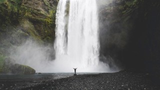 A huge waterfall in the background and a small figure standing at the bottom, raising their arms.