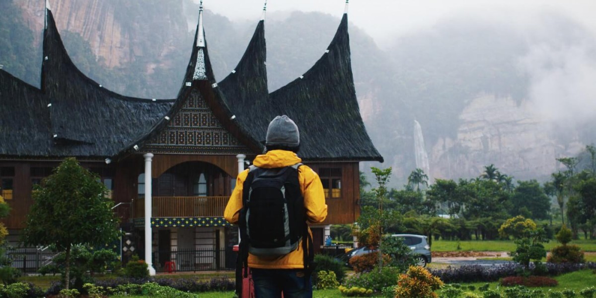 A hiker stands in front of an old asian building. Misty mountains in the background.
